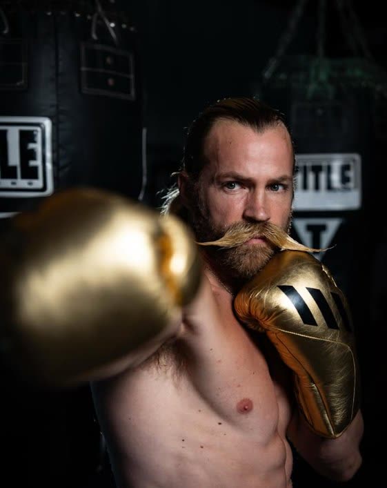 Brendan Kelly with gold boxing gloves in a TITLE boxing gym — professional boxer and elite multi-sport athlete